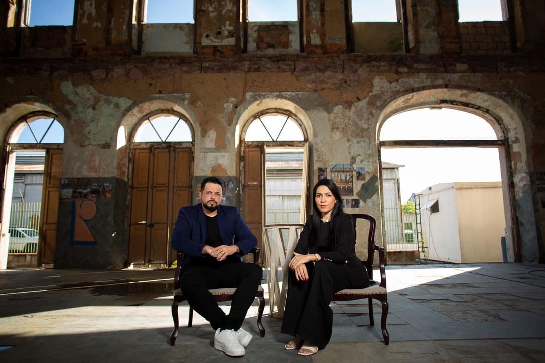 Roberto e Roberta sentados cada um numa poltrona, num galpão antigo